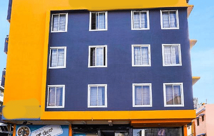A multi-story building with a blue and yellow facade, visible windows, and potted plants at the entrance | Astra Hotels and Suites Electronic City